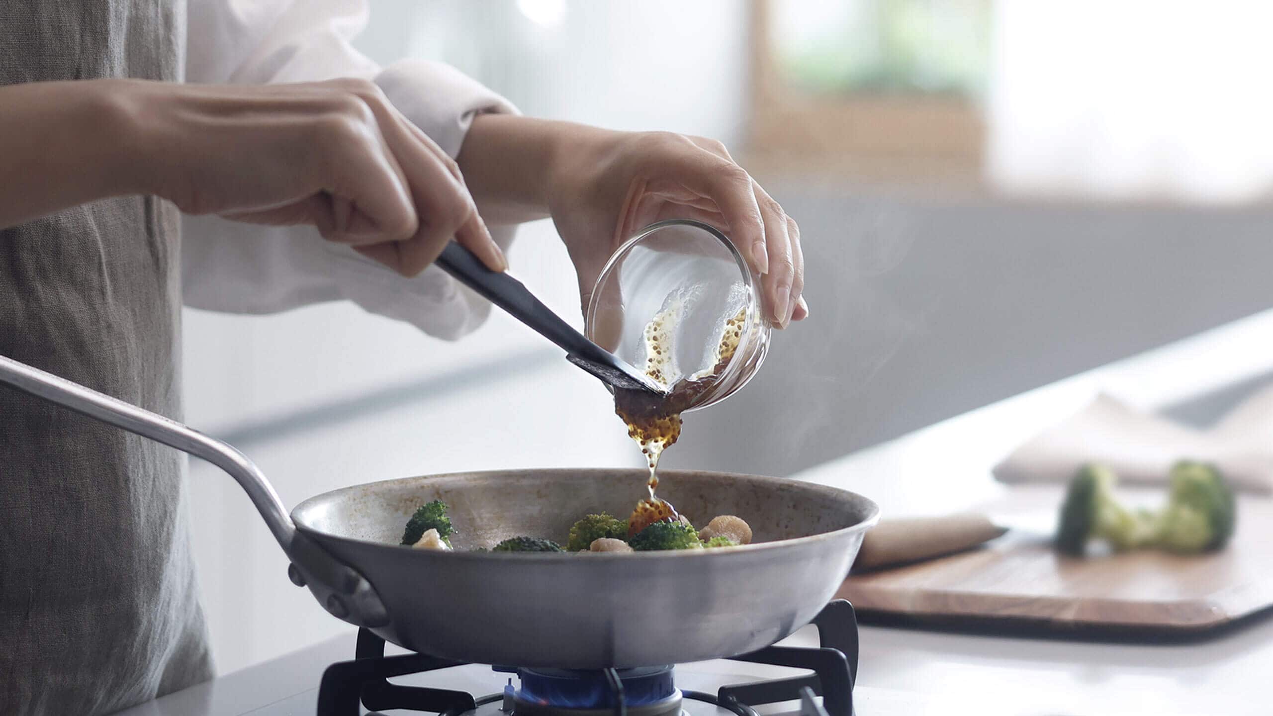容器の調味料をフライパンへ移す公式使用例。食材・鍋・容器は付属しません。